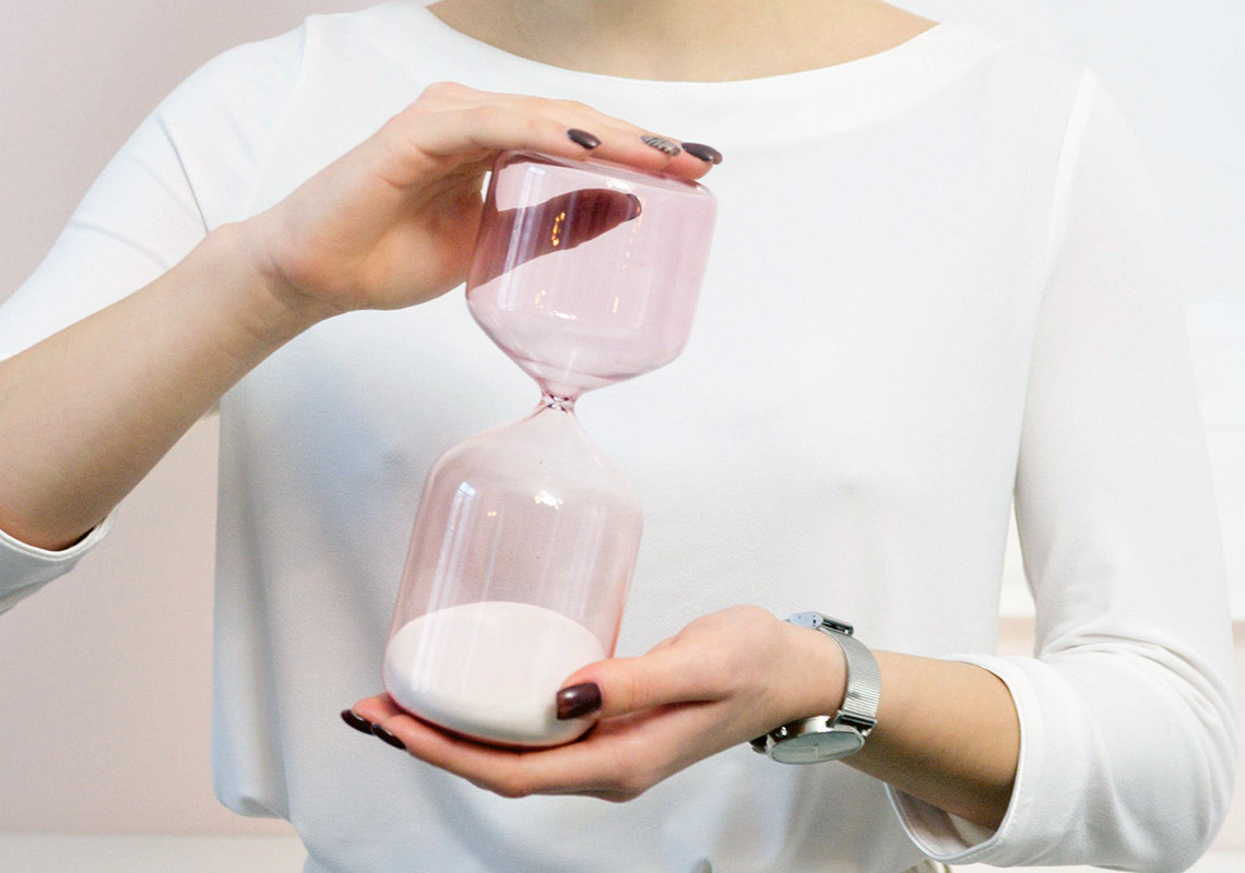 Behandlungsdauer Kieferorthopädie: Eine Frau hält eine rosa Sanduhr in der Hand.
