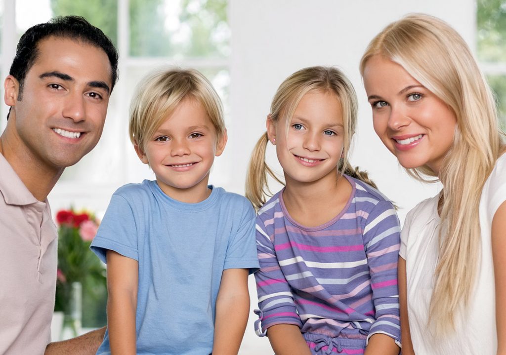 Eine junge Familie mit zwei Kindern blickt strahlend in die Kamera.
