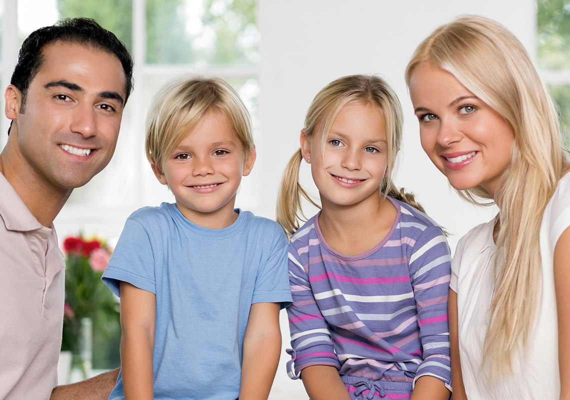 Eine junge Familie mit zwei Kindern blickt strahlend in die Kamera.